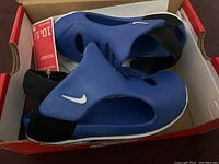 Pair of new Nike toddler sandals in size 10C, blue with black heel strap and white sole, inside original red and white Nike box, with tags attached.