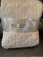 Front view of packaged beige queen size bed throw with diamond quilt pattern and label visible