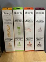 Front view of the four Abeego beeswax food wrap packages showing size and illustrations (baguette, asparagus, cheese wedge, onion).