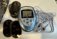 Mini TENS unit with black electrode pads and white connection wires displayed on white surface.