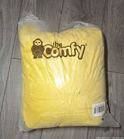 Photo of the yellow hooded blanket folded and sealed in its original plastic packaging with The Comfy logo.