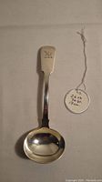 Front view of the silver ladle showing the engraved hallmark on the handle and its curved bowl.