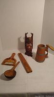 All five wooden items on a flat surface including Buddha, flute, beer stein, spoon, and mini broom