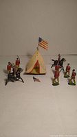 Photo showing the full set of painted lead soldiers, cavalry on horse, tent with American flag on top, and a detached small flag piece placed on the surface.