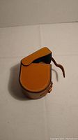 Small, tan leather flyfishing case partially open showing black felt interior and leather tie strap closure.