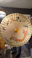 Photo of Japanese hand painted rice paper umbrella held open showing colorful bird and fish artwork and wooden ribs.