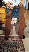 Full view of brown leather horse chaps held by a person showing size and shape