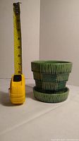 Green McCoy Pottery planter placed next to measuring tape showing height approx 6.5 inches, side view highlights textured vertical and horizontal lines on planter exterior and matching saucer below.