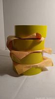 Stacked four rolls of yellow duct tape with some brown paper backing visible.