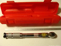 Front view of 1/4 inch drive torque wrench showing knurled handle and red case behind.
