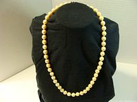 Full view of the pearl necklace displayed on black stand showing cream-colored round pearls knotted between each bead.