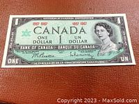 Front side of 1967 Canadian one dollar bill showing Queen Elizabeth II and centennial marks.