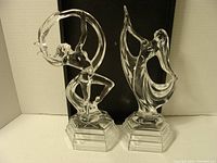 Two clear glass figurines shown side by side on a flat surface