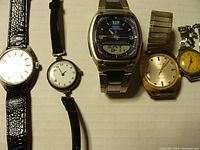 Five vintage watches lined up on a surface: two leather strap watches, one metal strap Casio watch, a gold-toned watch, and a small yellow dial watch.