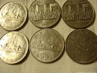 Six Canadian one dollar coins showing the obverse with Queen Elizabeth II profiles and the reverse with Voyageur and Constitution Day designs.