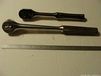 Top view showing both ratchets side by side with metal ruler beneath for scale. Husky ratchet has knurled handle; Armstrong ratchet has smooth handle.