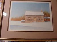 Framed limited edition print showing landmark log cabin in a winter landscape with snow and bare trees