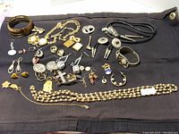 Overview of entire lot showing multiple bracelets, necklaces, charms, and earrings laid out on black fabric.