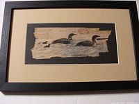 Full view of framed artwork featuring two adult loons and two chicks swimming, painted on natural birch bark with signature.