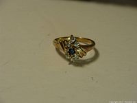 Close-up photo of a 10K gold ring with a central blue rhinestone and surrounding clear rhinestones on a smooth yellow gold band.