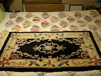 Full view of the oriental runner rug showing the floral border and central design on black background laid on a quilt.