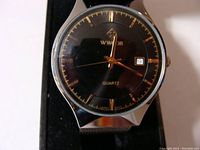 Close-up front view of WWOOR watch face showing black dial, gold hands, gold hour markers, date window, and silver tone case.