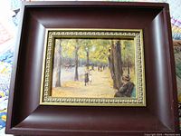 Framed oil painting depicting a shaded park path with trees and figures including a seated man and people walking with a child.