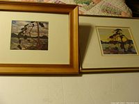 Pair of Group of Seven prints framed and matted, showing two landscape scenes with trees and lakes.