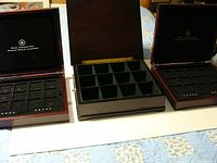 Three Royal Canadian Mint coin boxes open to show interior compartments for coin capsules and storage. One box missing handles.