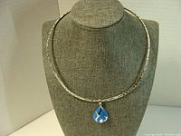 Full view of the choker necklace on display stand, showing textured silver and pendant.