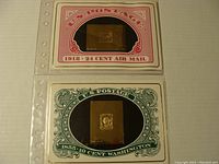 Two 23 karat gold stamps shown mounted in protective display holders resembling vintage U.S. postage stamps, one with red border from 1918 Air Mail issue, the other with green border from 1855 Washington issue.