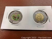 Reverse side views of both coins, one with colored Indigenous art and one standard metal design.
