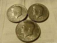 Obverse side of three Kennedy half dollar coins dated 1971, 1972, and 1977 showing profile of John F. Kennedy.