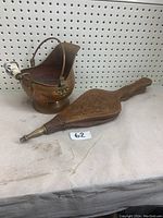 Copper ash bucket with porcelain-handled handle and wooden fireplace bellows with carved decorative patterns and brass nozzle, viewed from two angles