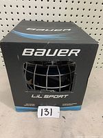 Front view of Bauer Lil'Sport youth hockey helmet in original box with cage visible through front window.