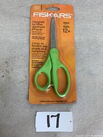 Green handle Fiskars scissors in original orange retail packaging showing front with age and project suitability labeling.