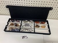 Black storage case opened showing eight pairs of NYS Collection sunglasses arranged in separate compartments.