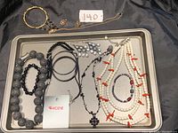 Photo of a collection of women's jewelry including necklaces, bracelets, and earrings displayed on a black background with a metal tray.