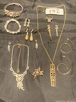 Full set of women's gold tone jewelry including multiple necklaces, bracelets, earrings, rings, and a hairpin arranged on black fabric.