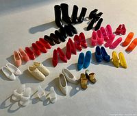 Top-down view of 27 matched pairs of Barbie footwear arranged by color and style showing diverse styles such as boots, pumps, flats, sandals, and sneakers.