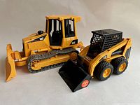 Two Bruder CAT toy construction vehicles, yellow with black details, a track-type tractor and skid steer loader.
