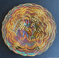 Top-down view of the carnival glass footed plate showing the scalloped edge and grape vine embossed design with iridescence.