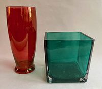 Two glass vases: one tall red cylindrical vase and one blue-green square vase side by side.