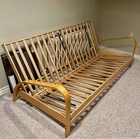 Full view of assembled futon frame convertible from sofa to bed position, natural wood finish with slats and curved arms.