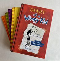 Five Diary of a Wimpy Kid hardcover books stacked showing front cover of first book with red cover and cartoon character illustration.