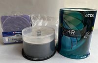 Photo of spindle of TDK DVD+R 100 discs sealed, opened spindle of TDK DVD+RW, and purple Verbatim CD/DVD sleeves