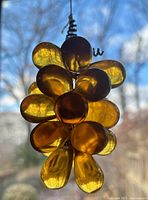 Close-up photo of amber-coloured glass grape-shaped beads clustered on black coiled wire vine against sky background showing translucency and color.