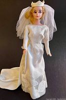 Front view of the Barbie-size doll wearing the white bridal gown with fitted bodice, long sleeves, and crown with attached veil.