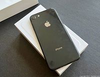 iPhone 8 steel grey phone shown from back side on top of white box, minor wear visible on back cover.