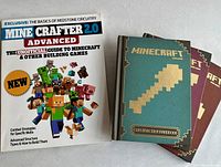 Four Minecraft-related books displayed: three official hardcovers and one unofficial paperback guide with Minecraft characters on cover.